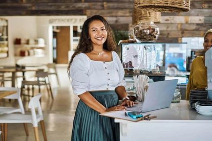 A server smiling and standing by the counter on her laptop