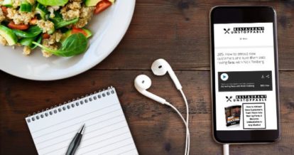 Image of a table surface with a phone playing a podcast called Restaurant Unstoppable, earphones, a salad, and pen and paper