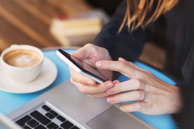 A woman on her phone with a latte and laptop at the table