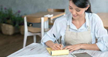 A woman sitting at a table writing on a pad and paper.