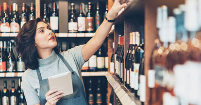 a staff member with a pad of paper in the cellar touching a bottle of wine on the shelf.
