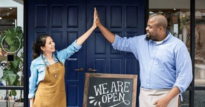 2 restaurant employees high five in front of their restaurant with a 