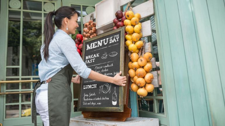 woman setting up sandwich board outside shop