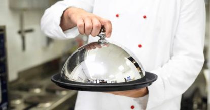 A chef serving a covered plate