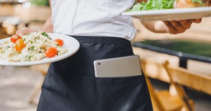 Server dropping meals to table with iPad POS tucked in apron pocket
