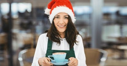 A woman holding a tea cup filled with coffee with a Christmas hat on.