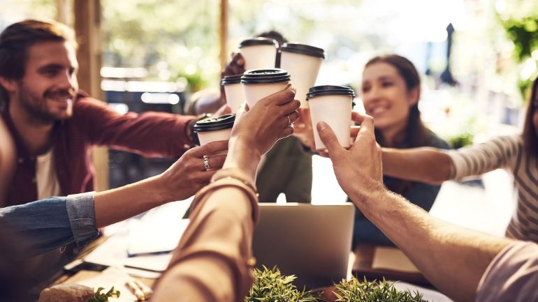 Six people at a restaurant toasting takeout coffee cups at the center of a table