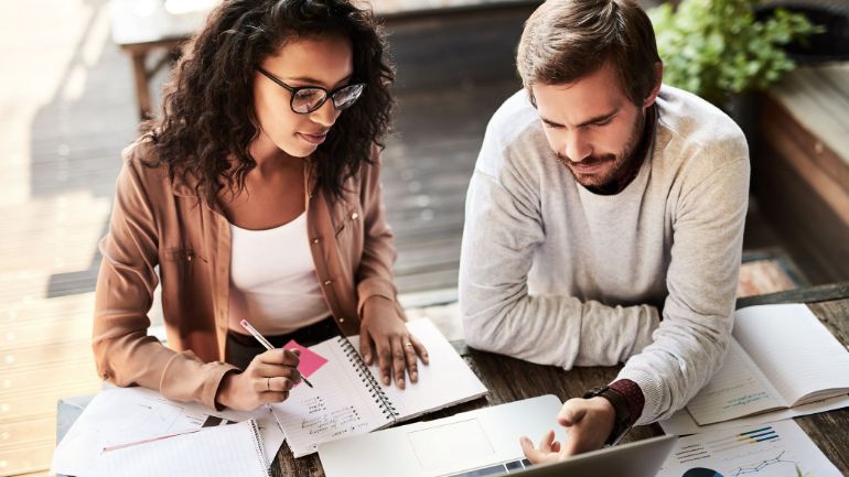 Woman wearing glasses doing paperwork and a bearded man looking at restaurant sales numbers