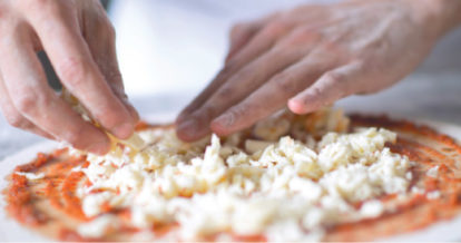 Chef spreading cheese on a pizza