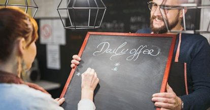 A man holding up chalkboard as a woman writes on it