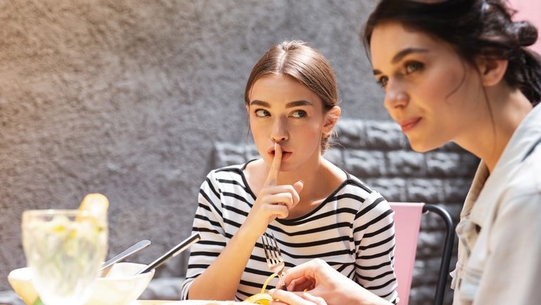 Woman whispering to another woman about leaving the restaurant without paying.