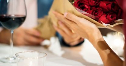 Person handing a bouquet of roses to another at a restaurant table