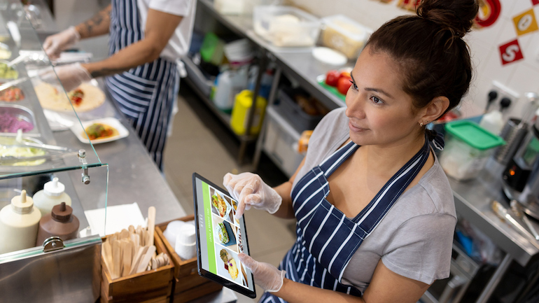 Woman working at a restaurant taking an order on a tablet.