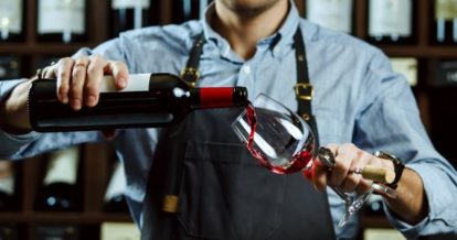 A man in an apron pouring wine into a glass