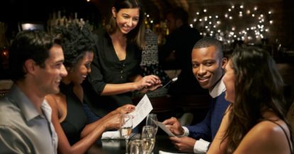 Four friends sitting at a restaurant having a good time as the waiter takes thier order.