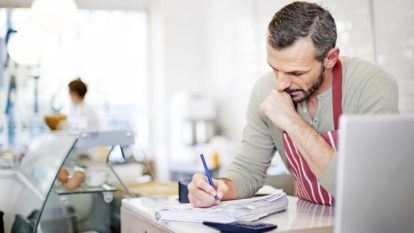 Man sitting in restaurant writing on pad with pencil, working on cash flow management plan