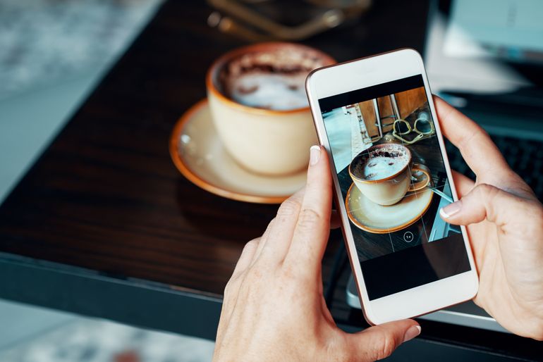 Person taking photo of cappucino, part of social media marketing for restaurants