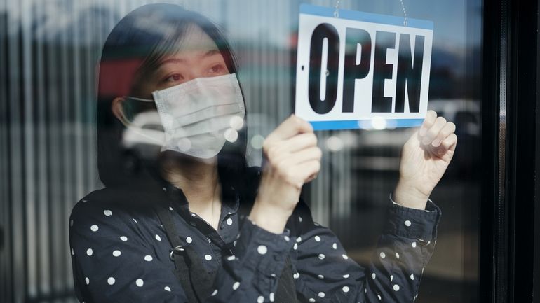 Woman wearing a face mask hanging an "open" sign in a restaurant window