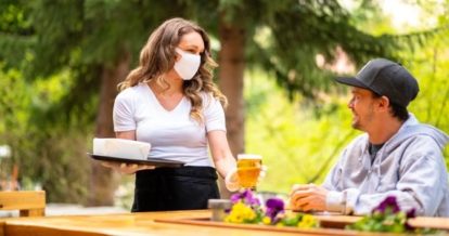 Server wearing a face mask handing a man a beer on an outdoor patio