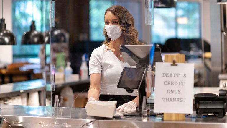 Cashier wearing a mask placing a takeout container on a counter