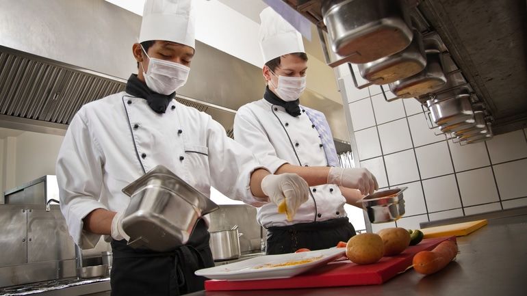 Two chefs wearing masks while cooking in a restaurant kitchen