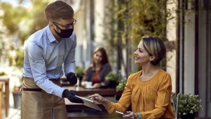 Waiter wearing a mask while showing a menu to a woman on a patio