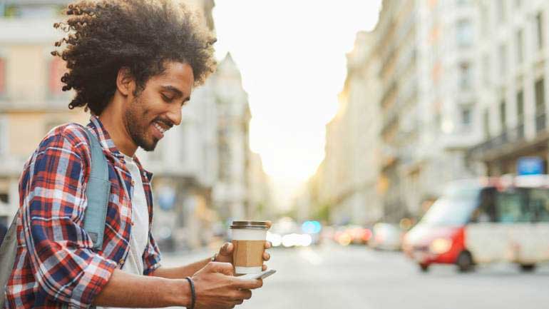 A man walking while texting and hold a coffee in his other hand