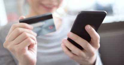 A woman holding a payment card in one hand and a mobile phone in the other hand