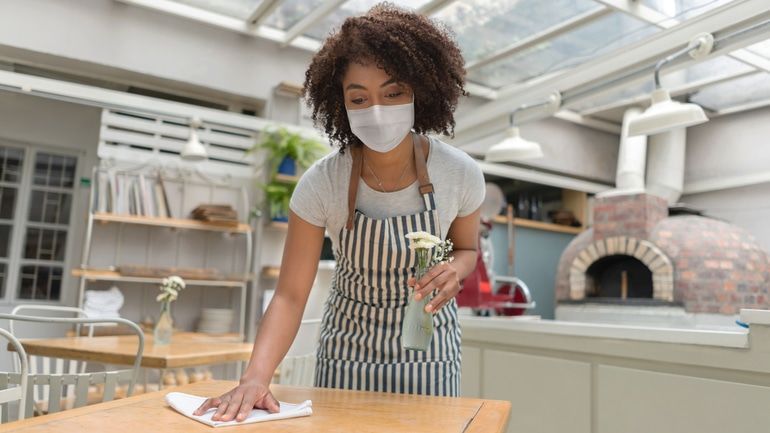 Waitress at a restaurant wearing a facemask and disinfecting the tables