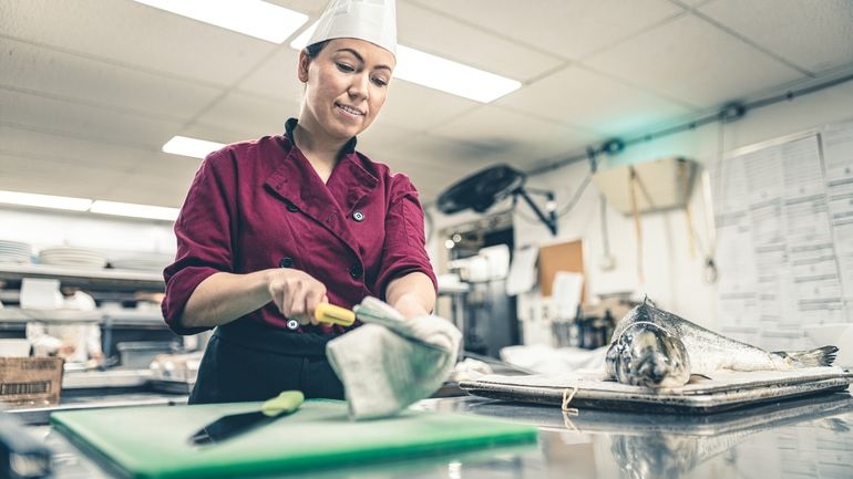 Female chef working in industrial kitchen and cleaning a knife