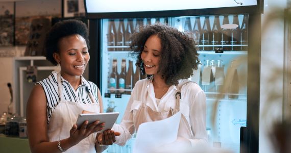 2 restaurant employees holding iPad and papers in front of a restaurant beverage fridge