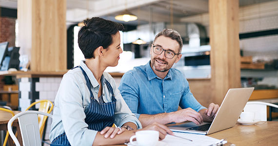 Restaurant employees sitting at a table in a restaurant with laptop, paperwork, and coffee