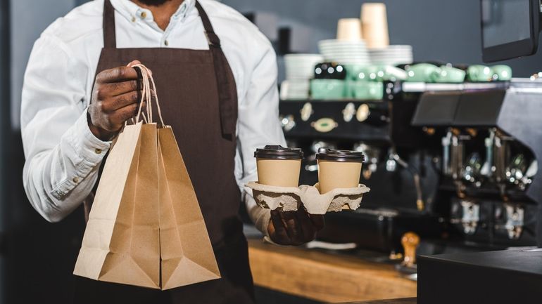 Barista holding tray of takeaway coffee and brown paper bags