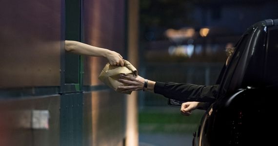 Restaurant employee handing takeout bag to customer inside a car