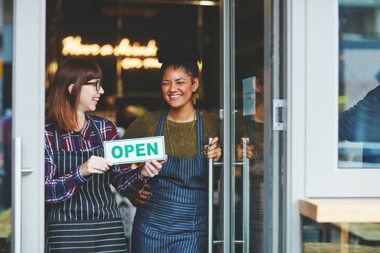 two restaurant staff holding their "open" sign