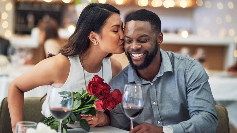 Woman with flowers kissing a man on the cheek in a restaurant.