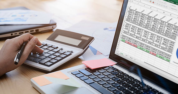 A laptop screen showing financial profit and loss and a hand tapping numbers on a calculator