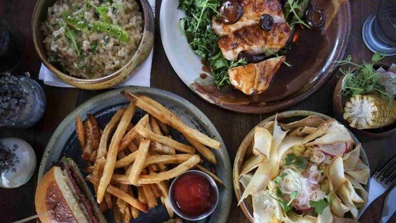 Spread of food at Miami restaurant Pinch Kitchen, including a burger, fries, dip, and chicken breast