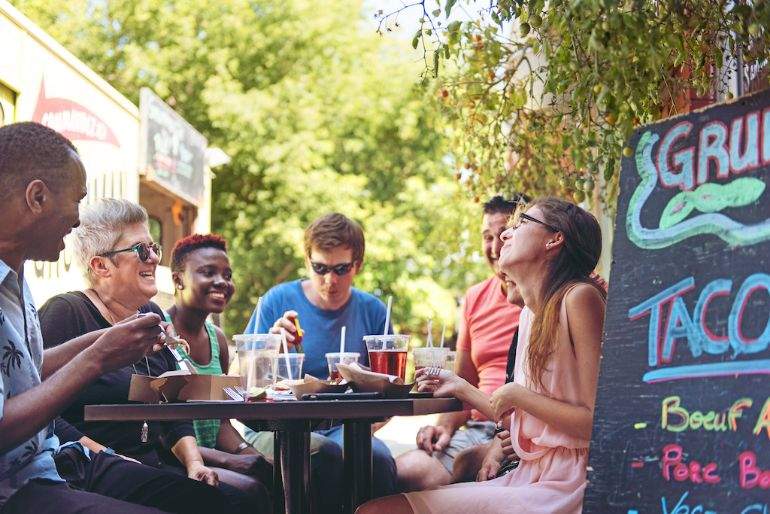 Friends gathered at a picnic table eating and drinking beside a food truck