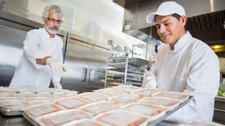 Back of house staff organizing sheet pans of individually wrapped meals