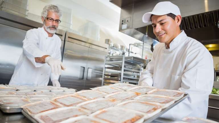 Back of house staff organizing sheet pans of individually wrapped meals