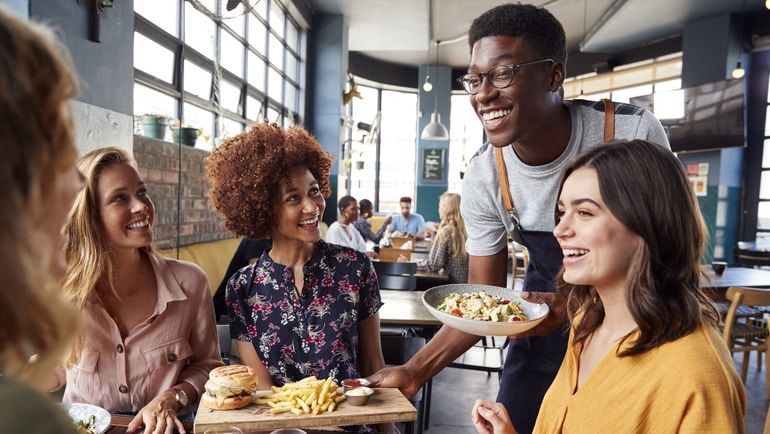 A smiling server delivering food to a table of diners