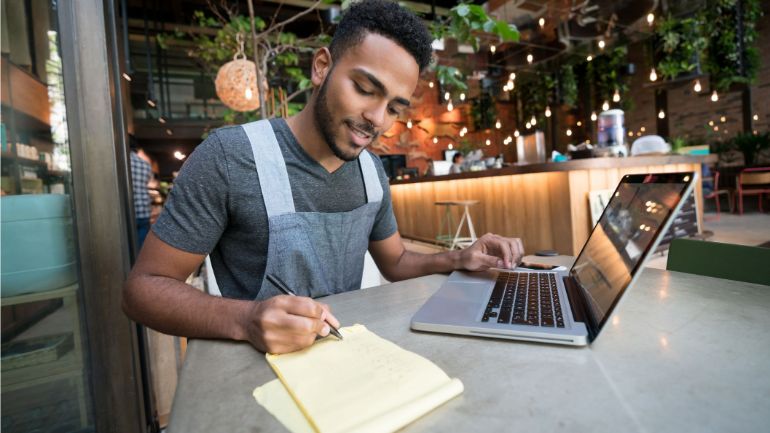 Restaurant manager with laptop making notes on a notepad