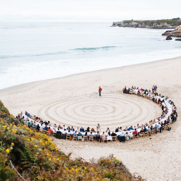 Diners sitting in a large semi circle on a sandy beach.