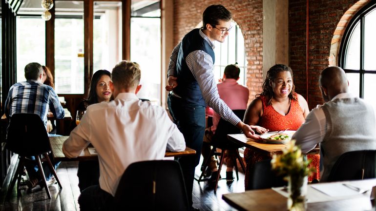 Server delivering plate of food to pair of diners