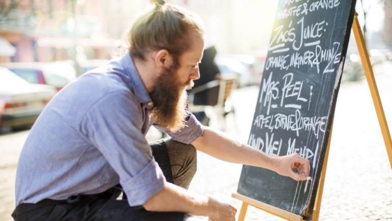 cafe worker filling specials on a sidewalk chalkboard