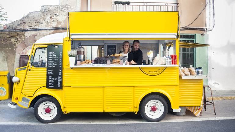 two business owners smiling from inside their yellow food truck