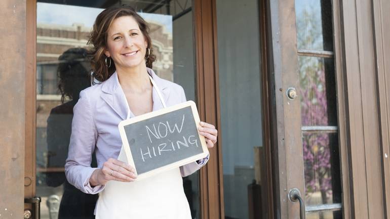 A restaurant owner holding up a "Now Hiring" sign.