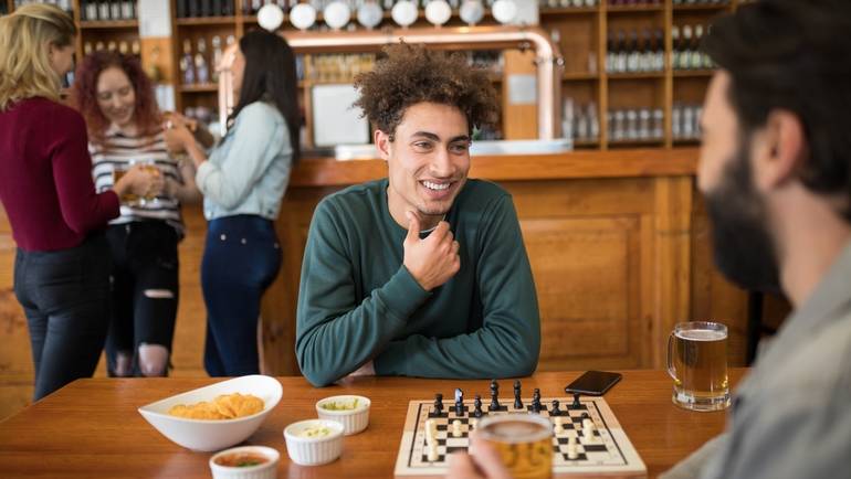 two friends having snacks, beer and playing chess