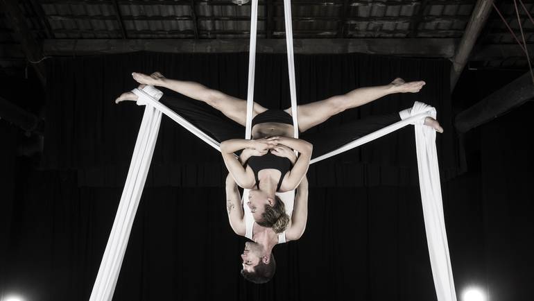 two acrobats hanging upside down from silks